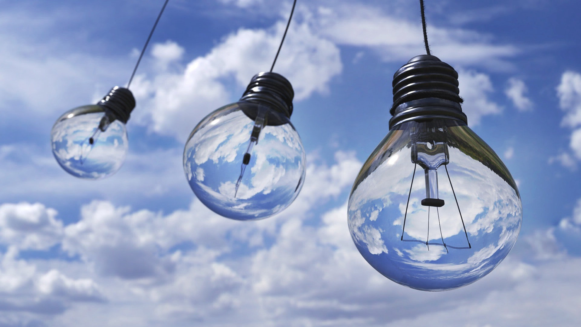 Three transparent lightbulbs in front of a blue cloudy sky